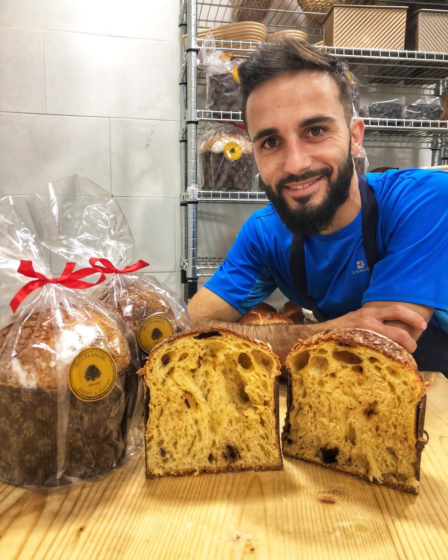 Panadero sonriente con panettones, uno cortado mostrando el interior de masa aireada con chispas de chocolate